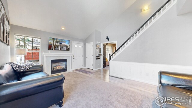 carpeted living area with stairs, vaulted ceiling, a fireplace with flush hearth, baseboards, and recessed lighting