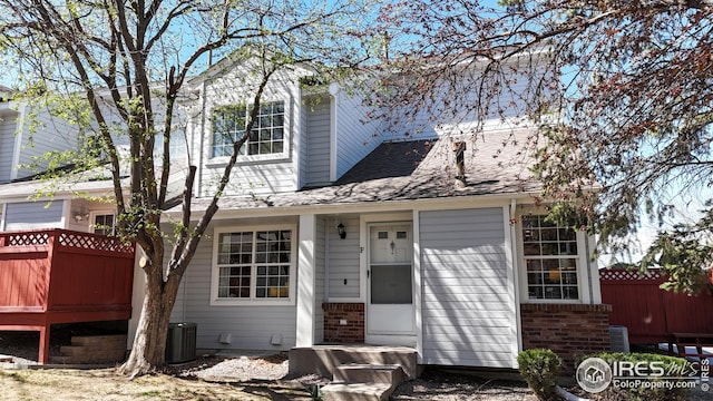 traditional-style home with brick siding, central air condition unit, fence, and roof with shingles