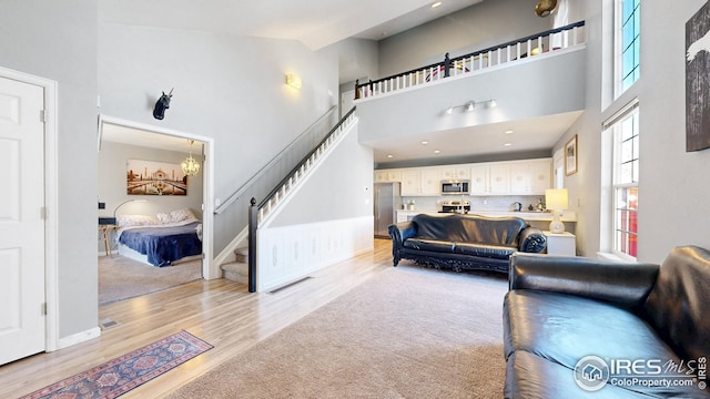 living area featuring a notable chandelier, stairway, light wood-style flooring, baseboards, and a towering ceiling