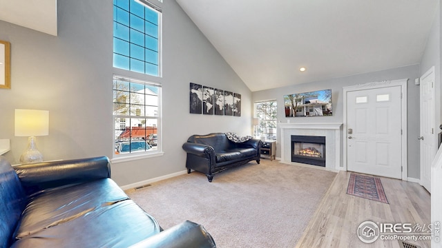carpeted living room with high vaulted ceiling, plenty of natural light, a fireplace with flush hearth, and visible vents