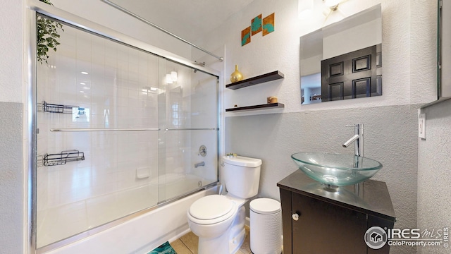 bathroom featuring combined bath / shower with glass door, tile patterned floors, toilet, vanity, and a textured wall