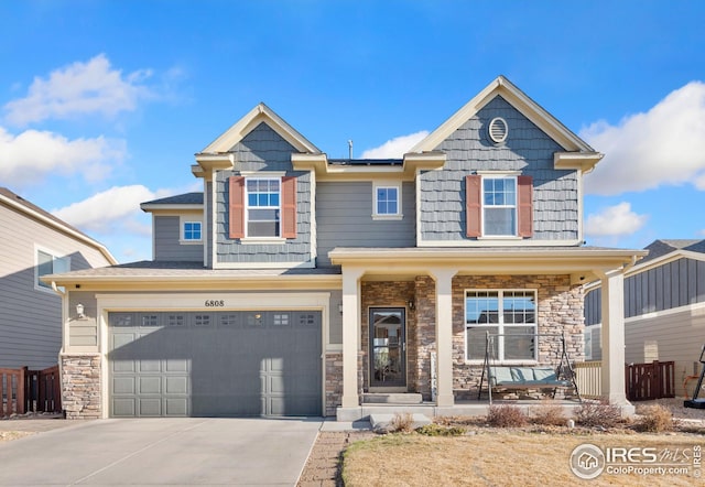 craftsman house featuring stone siding, concrete driveway, an attached garage, solar panels, and a porch
