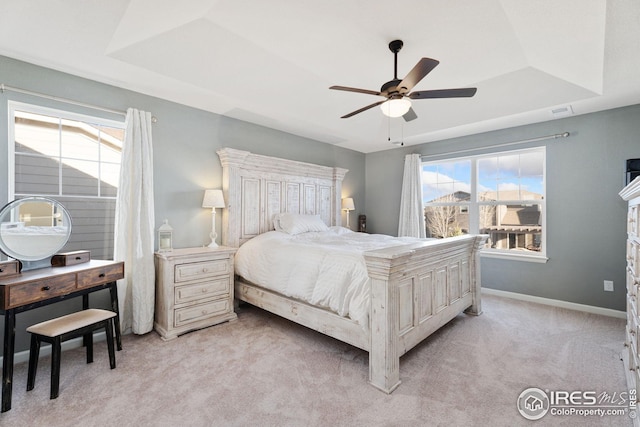 bedroom with a tray ceiling, light colored carpet, baseboards, ceiling fan, and visible vents