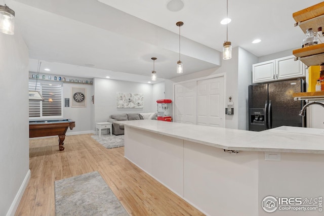 kitchen with white cabinetry, black fridge with ice dispenser, a sink, light wood-style flooring, and light stone countertops