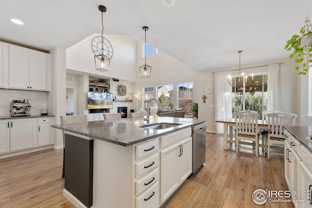 kitchen featuring a large fireplace, stainless steel dishwasher, a sink, light wood-style floors, and backsplash