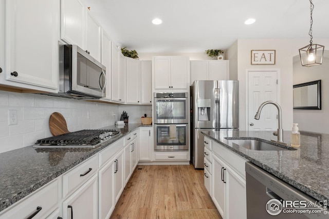 kitchen with a sink, light wood finished floors, white cabinetry, appliances with stainless steel finishes, and decorative backsplash