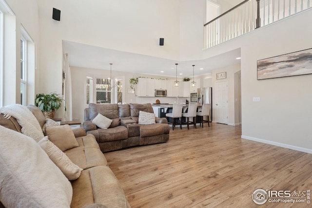 living area featuring baseboards, recessed lighting, light wood-style floors, a high ceiling, and a notable chandelier