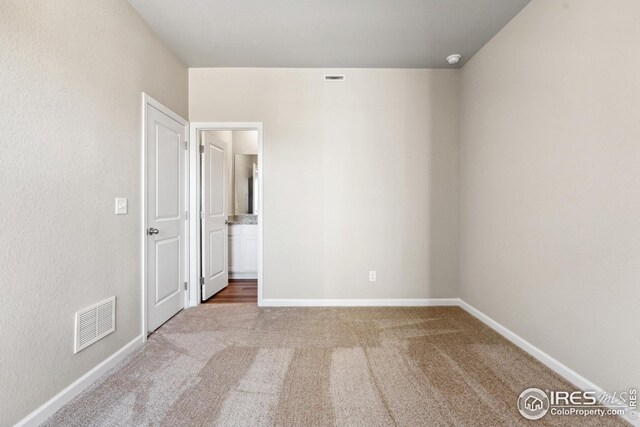 unfurnished bedroom with ensuite bathroom, carpet, baseboards, and visible vents