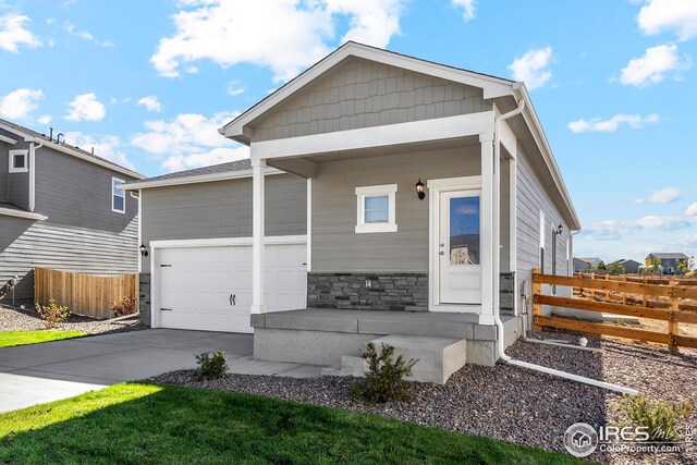 view of front facade with stone siding, fence, a garage, driveway, and covered porch