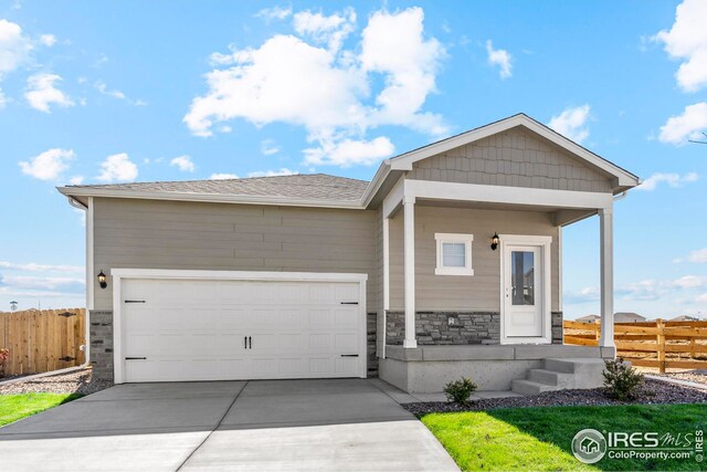 view of front of property with stone siding, a garage, fence, and concrete driveway