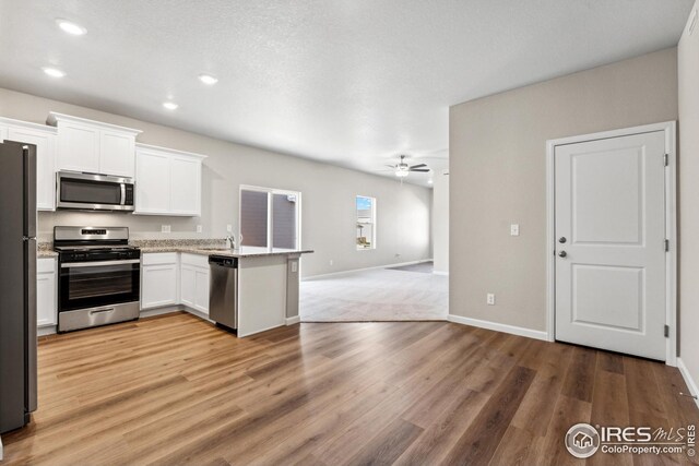 kitchen with white cabinets, a peninsula, ceiling fan, stainless steel appliances, and open floor plan