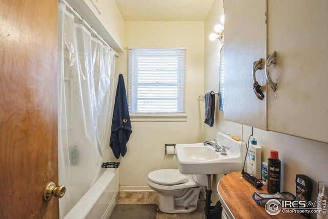 full bathroom with baseboards, toilet, shower / tub combo with curtain, and a sink