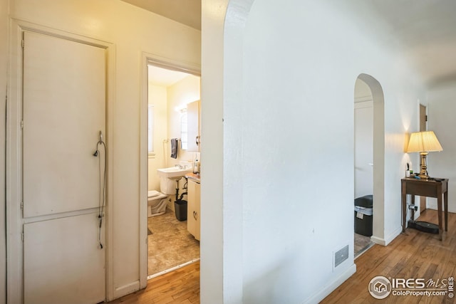 hallway featuring arched walkways, baseboards, and light wood-type flooring
