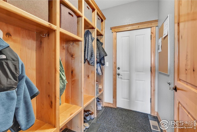 mudroom featuring dark tile patterned floors, baseboards, visible vents, and a textured wall