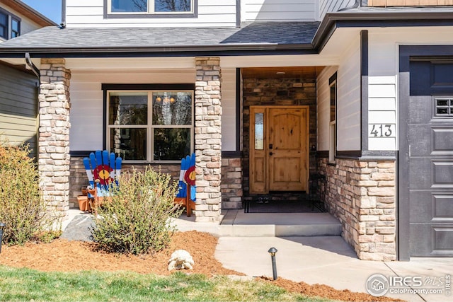 entrance to property featuring roof with shingles, a porch, and stone siding