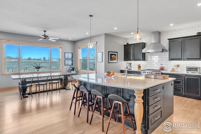 kitchen with a sink, light wood-style floors, tasteful backsplash, wall chimney exhaust hood, and a breakfast bar area
