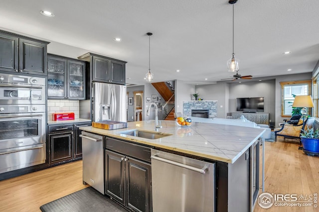kitchen with appliances with stainless steel finishes, a warming drawer, ceiling fan, a stone fireplace, and a sink