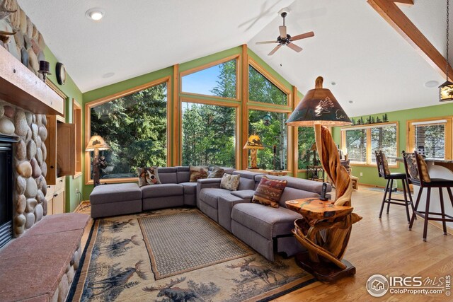 living area featuring light wood finished floors, a fireplace, lofted ceiling, and a ceiling fan