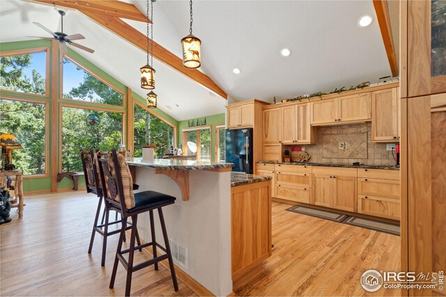 kitchen with beam ceiling, freestanding refrigerator, light wood finished floors, a kitchen bar, and light brown cabinets