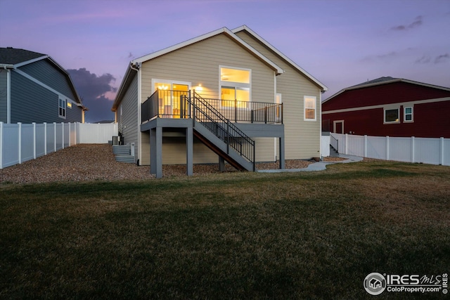 back of property at dusk featuring a lawn, a fenced backyard, stairway, and a deck
