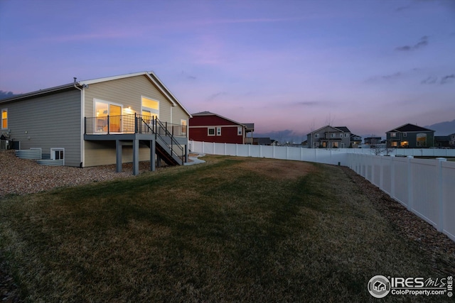 yard at dusk featuring a fenced backyard, stairway, and a deck