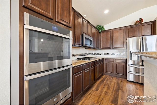 kitchen with light stone countertops, dark wood finished floors, lofted ceiling, stainless steel appliances, and decorative backsplash