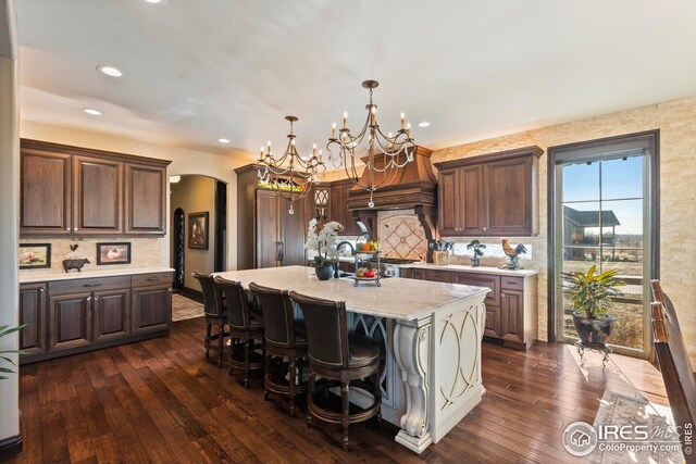 kitchen with dark wood-style flooring, a chandelier, arched walkways, a breakfast bar area, and backsplash