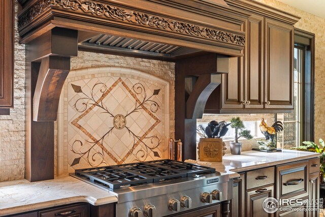 kitchen featuring stainless steel gas cooktop, light stone counters, premium range hood, stove, and decorative backsplash