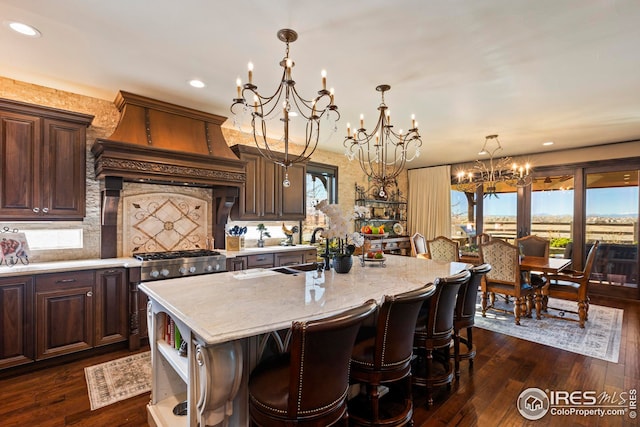 kitchen featuring dark wood-type flooring, custom range hood, a notable chandelier, and a center island with sink
