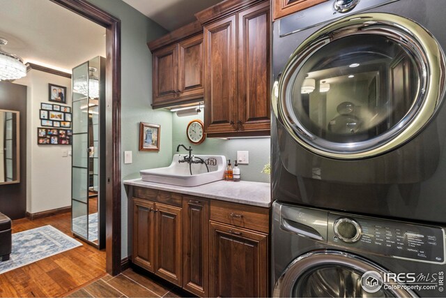 washroom with dark wood-type flooring, stacked washing maching and dryer, baseboards, a sink, and cabinet space