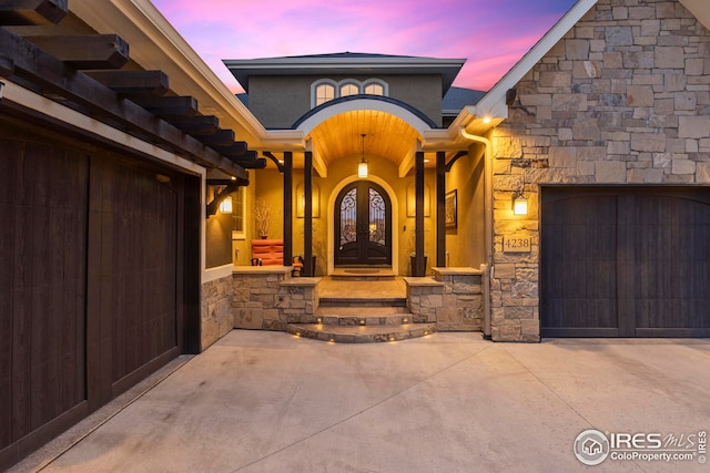 property entrance featuring stucco siding, french doors, stone siding, driveway, and a garage