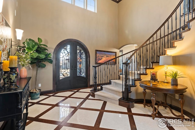 entryway featuring baseboards, arched walkways, french doors, and stairs