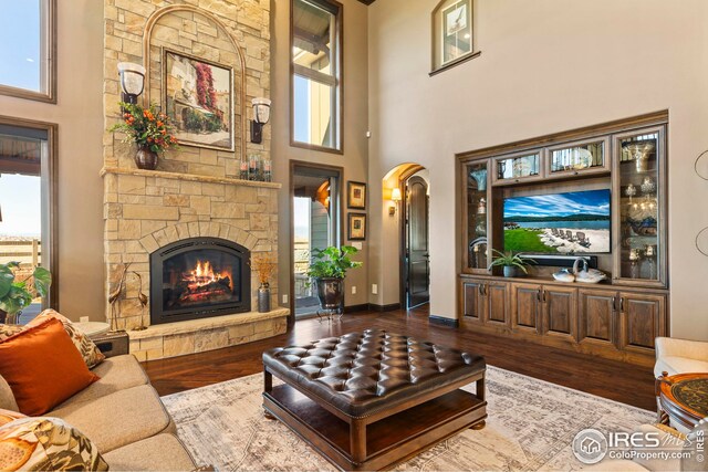 living area with a fireplace, wood finished floors, baseboards, arched walkways, and a towering ceiling
