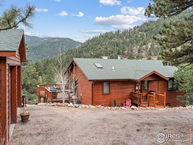 back of house featuring a view of trees, a deck with mountain view, and roof with shingles