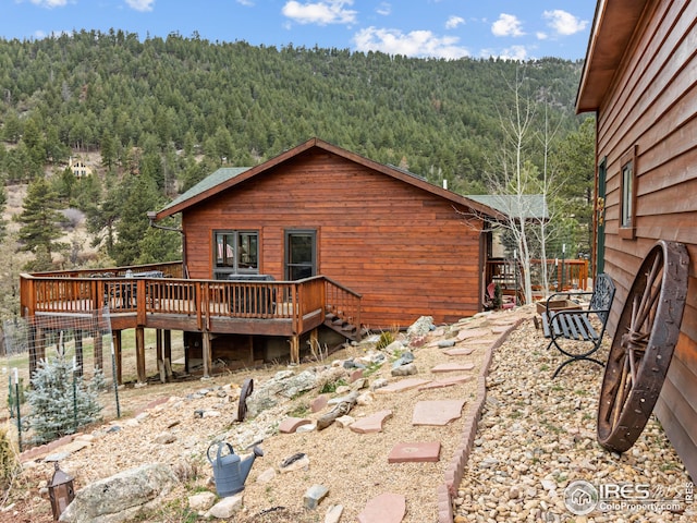 back of property featuring a view of trees and a wooden deck