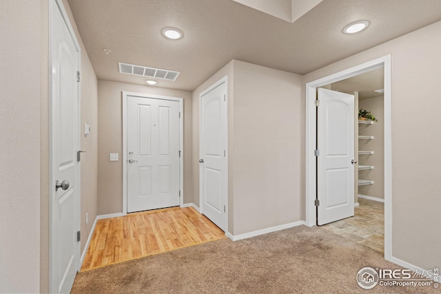 foyer entrance featuring baseboards, visible vents, carpet, and a textured ceiling