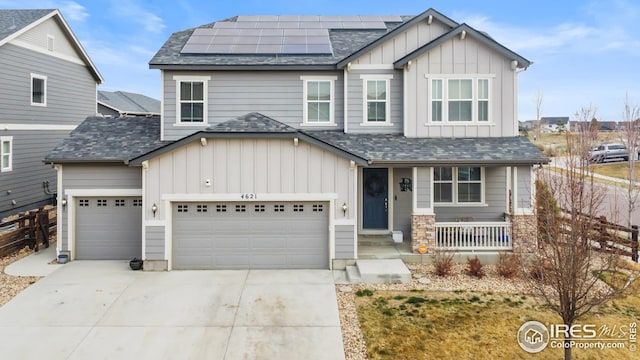craftsman-style home featuring board and batten siding, covered porch, concrete driveway, solar panels, and a shingled roof