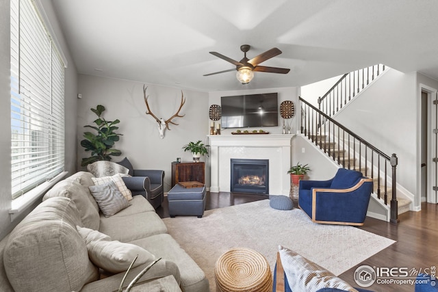 living area featuring ceiling fan, a glass covered fireplace, stairway, and wood finished floors
