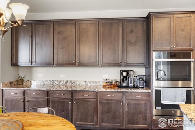 kitchen featuring stainless steel double oven, light stone counters, and dark brown cabinetry
