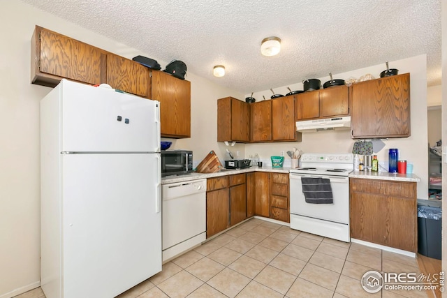 kitchen featuring light countertops, white appliances, light tile patterned floors, under cabinet range hood, and brown cabinets