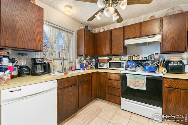 kitchen with a textured ceiling, light countertops, white appliances, under cabinet range hood, and a sink