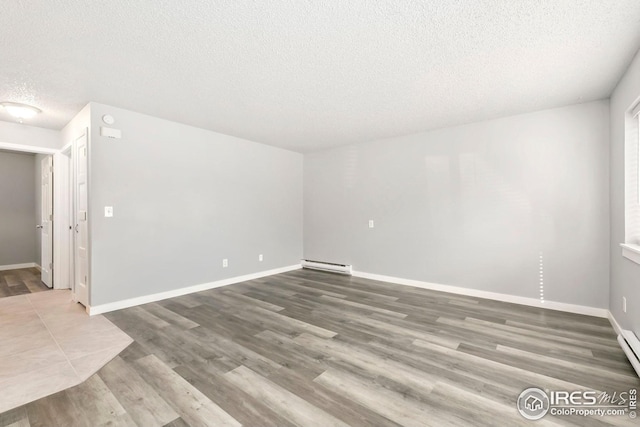unfurnished room featuring baseboards, wood finished floors, and a baseboard heating unit