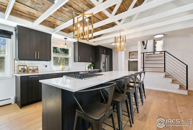 kitchen featuring decorative backsplash, light wood-style flooring, beamed ceiling, appliances with stainless steel finishes, and a notable chandelier