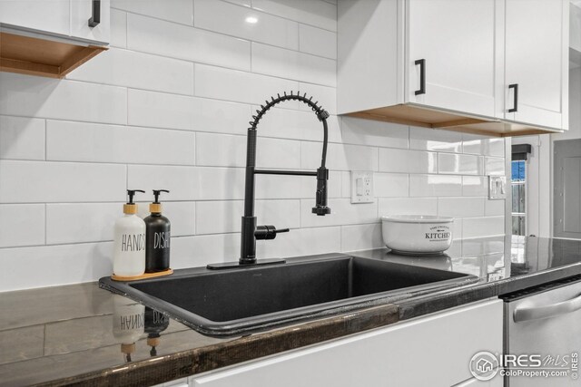 kitchen featuring tasteful backsplash, dark countertops, a sink, dishwasher, and white cabinets