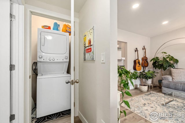 laundry area with baseboards, wood finished floors, stacked washer / dryer, and laundry area