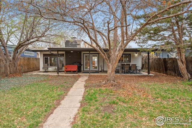 back of house with a fenced backyard, a chimney, a patio, and a lawn