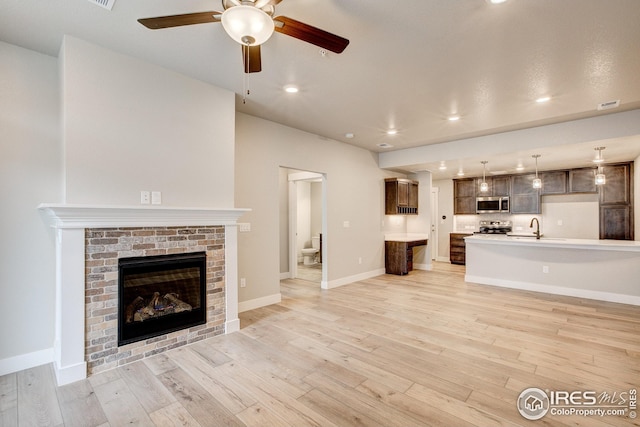 unfurnished living room with ceiling fan, a fireplace, visible vents, a sink, and light wood finished floors