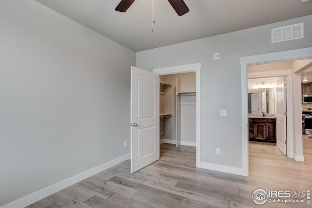 unfurnished bedroom featuring a closet, baseboards, light wood-style flooring, a walk in closet, and visible vents