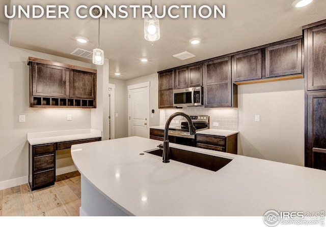 kitchen featuring a sink, light wood-style floors, dark brown cabinetry, stainless steel microwave, and backsplash