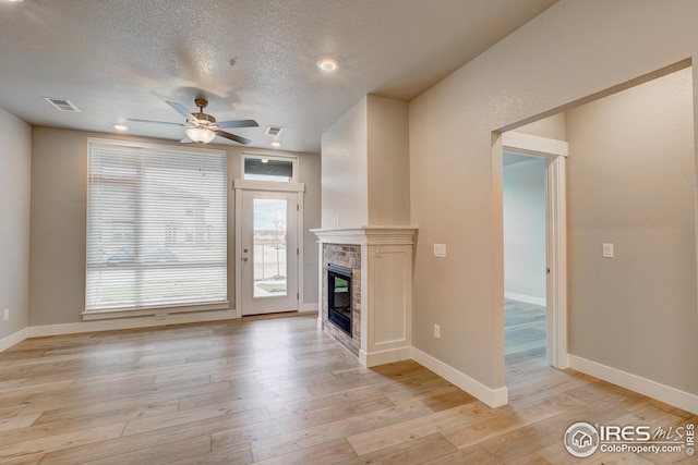 unfurnished living room featuring visible vents, ceiling fan, light wood-style floors, a textured ceiling, and a glass covered fireplace